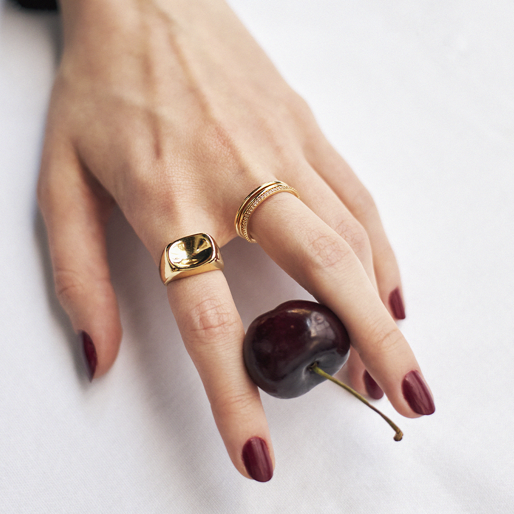 Anel Nixie Dourado combinado com aros finos e anel largo polido.